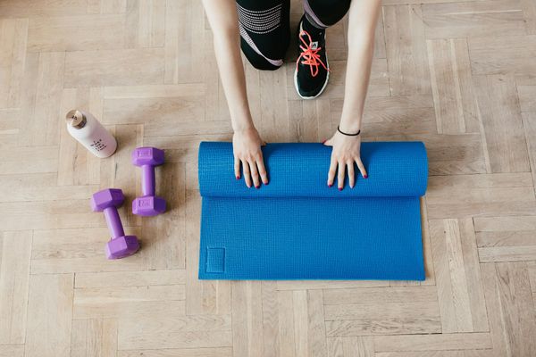 A neatly rolled yoga mat and a water bottle on a wooden floor.